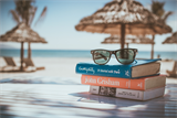 Strand mit Strohsonnenschirmen und Bücher und Sonnenbrille im Vordergrund